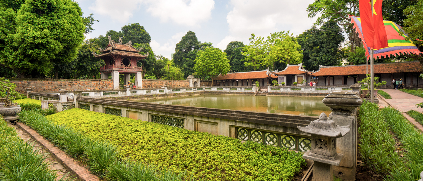 Historic temple grounds in Hue featuring a tranquil pond, traditional architecture, and vibrant green foliage.