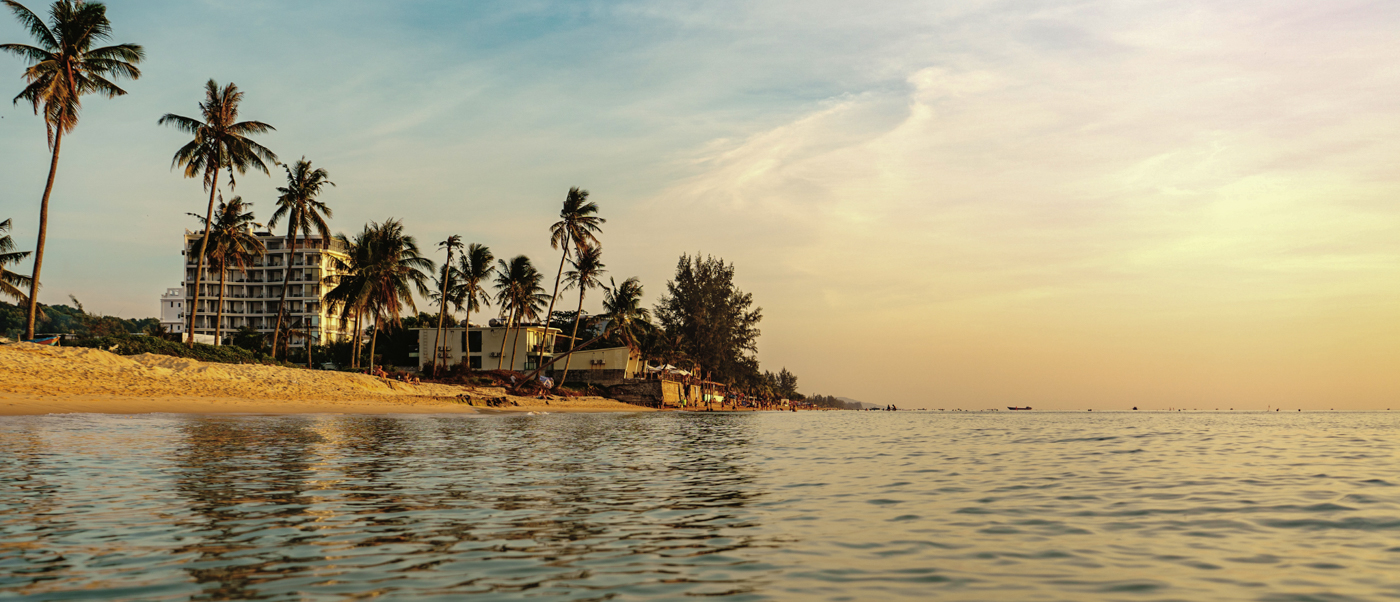 A serene tropical beach at sunset with palm trees, resorts, and calm ocean waters in Phu Quoc.