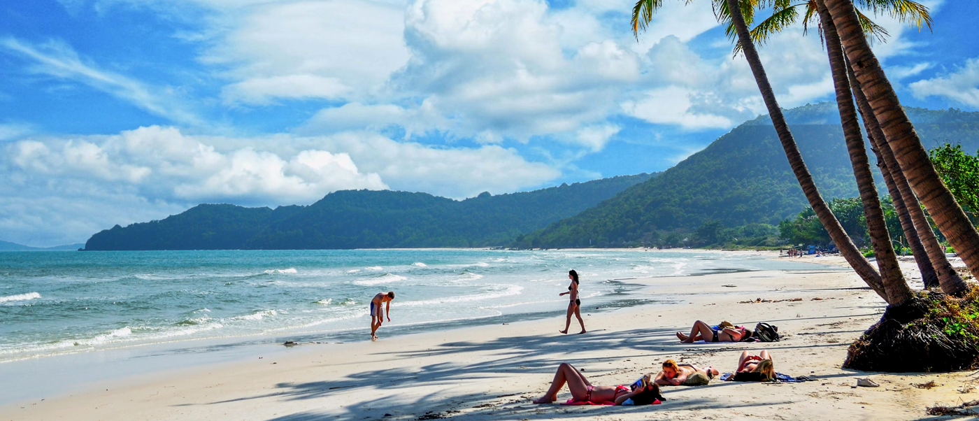 Tourists relax and stroll on a pristine sandy beach with palm trees and green mountains in Phu Quoc.