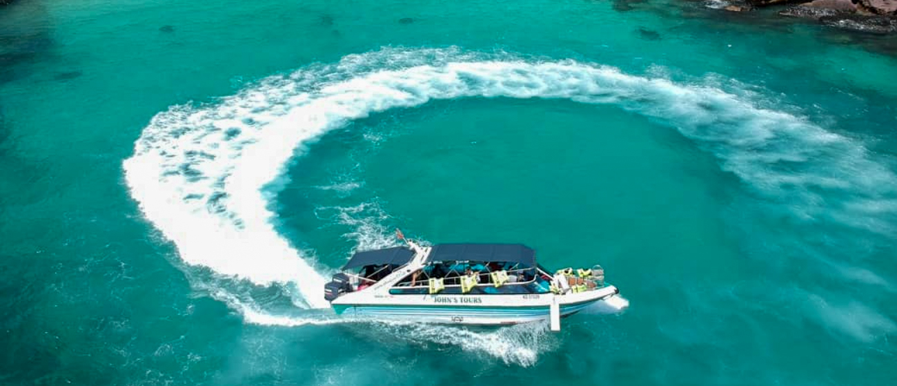 A tour boat makes a circular wake in the clear turquoise waters of Phu Quoc, Vietnam.