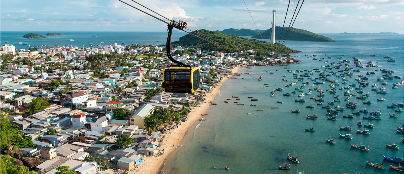 A cable car glides over the bustling coastal town and bay filled with fishing boats in Phu Quoc.