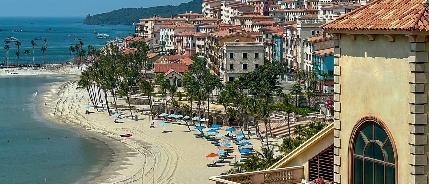 Idyllic Phu Quoc beach with rows of palm trees, beach umbrellas, and colorful Mediterranean-style buildings.