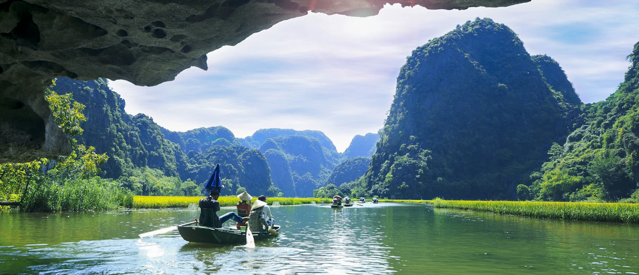 People on sampan boats explore a tranquil river surrounded by majestic karstic mountains in Tam Coc.