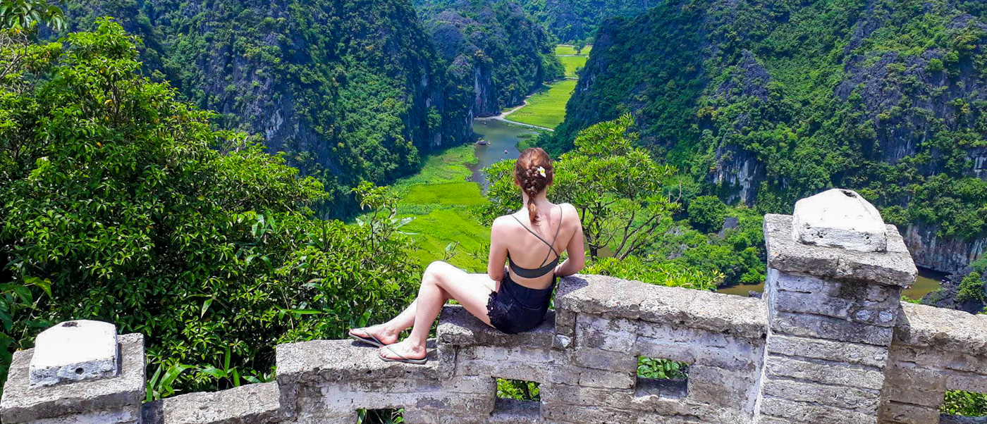 Woman sits on a viewpoint wall, admiring the sweeping green valley and winding river in Tam Coc.
